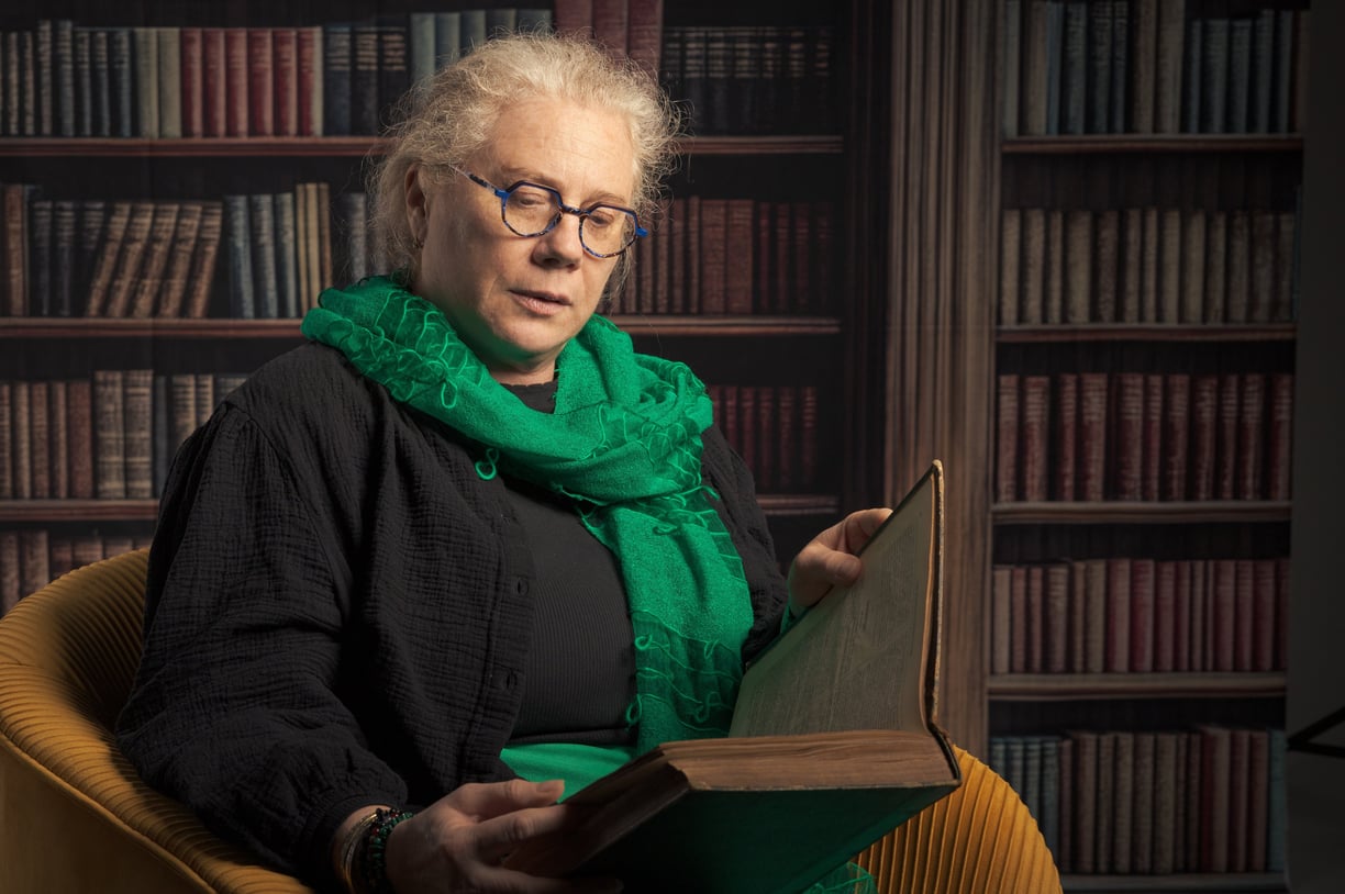 Femme sénior lisant un vieux livre dans fauteuil jaune, fond bibliothèque