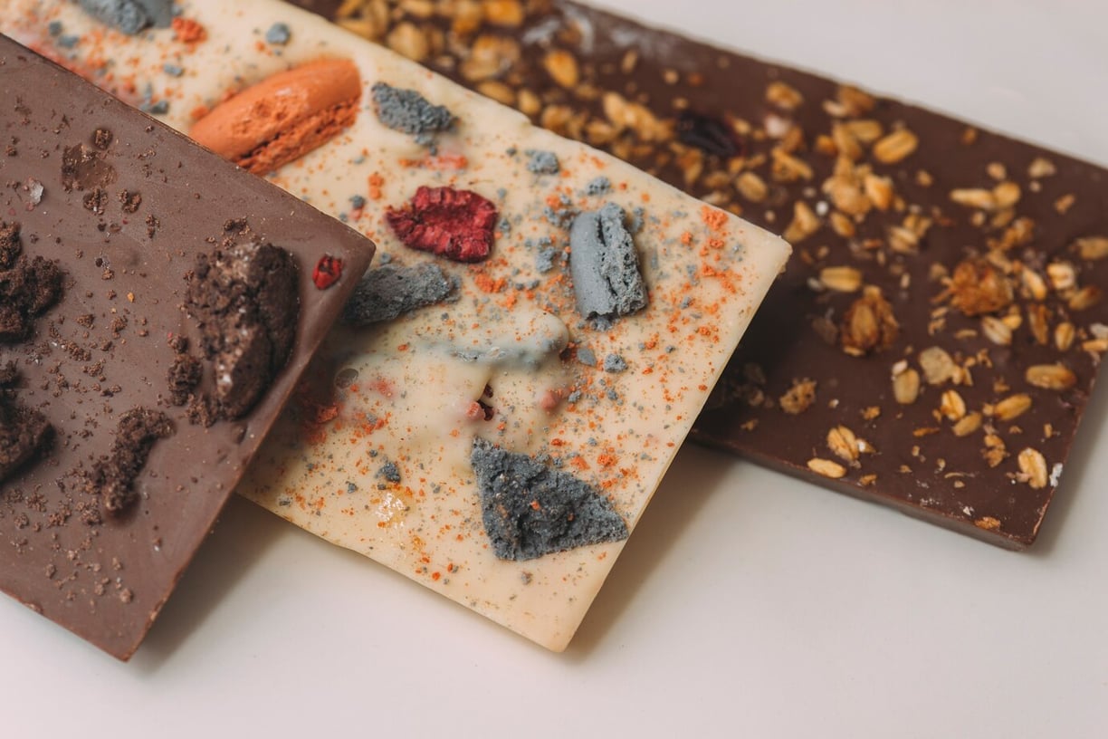 3 overlapping chocolate bars with toppings. Milk, white, & dark chocolate with colorful macaroon nut