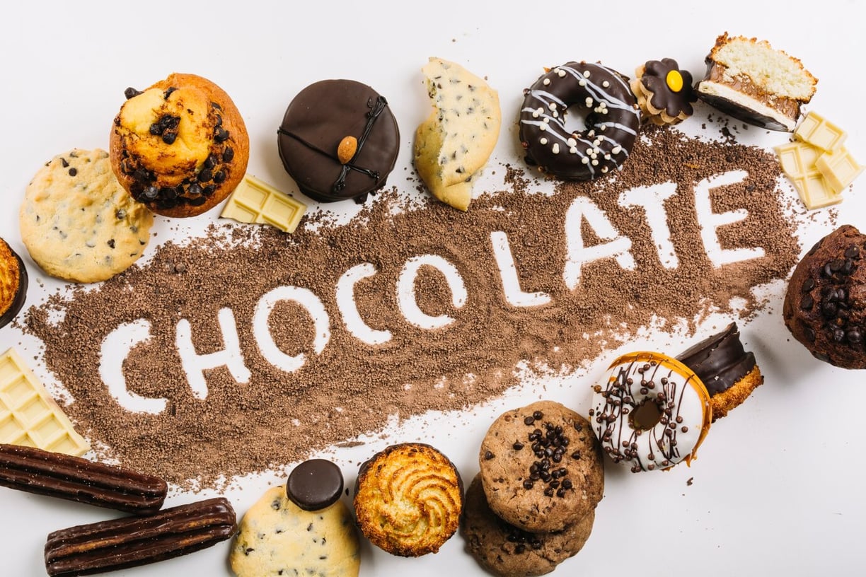Chocolate written in cocoa powder surrounded by chocolate baked goods: muffin, donut, churro, cookie