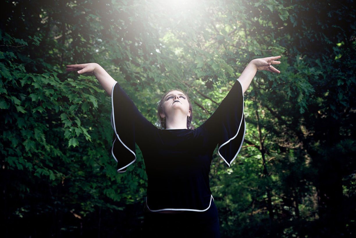 a woman with her arms outstretched up and she is looking up to the sun in the forest