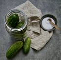 a jar of small cucumbers with a bowl of salt and a linen cloth