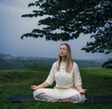 a woman sitting on a mat mat in a field doing meditation