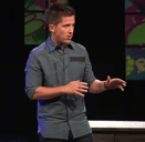a man standing on a stage speaking to a crowd