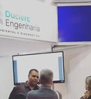Representante da Duclerc Engenharia atendendo cliente durante feira técnica, apresentando serviços d