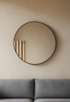 Round mirror with a thin black frame hanging above a modern grey couch.