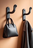 Two matte black wall hooks holding a black handbag and grey coat against a peach wall.