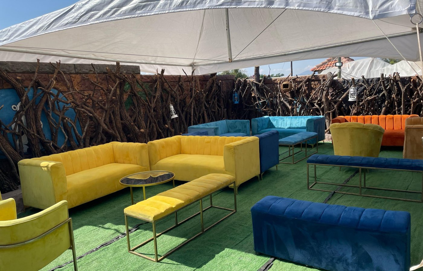 Outdoor lounge under a white marquee with mustard, blue and orange velvet sofas on artificial lawn