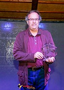 a man in a purple shirt and jeans standing in front of a blackboard