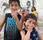 two young children standing in front of a wall with graffiti