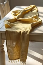 Yellow cheesecloth table runner draped over a light wooden table.