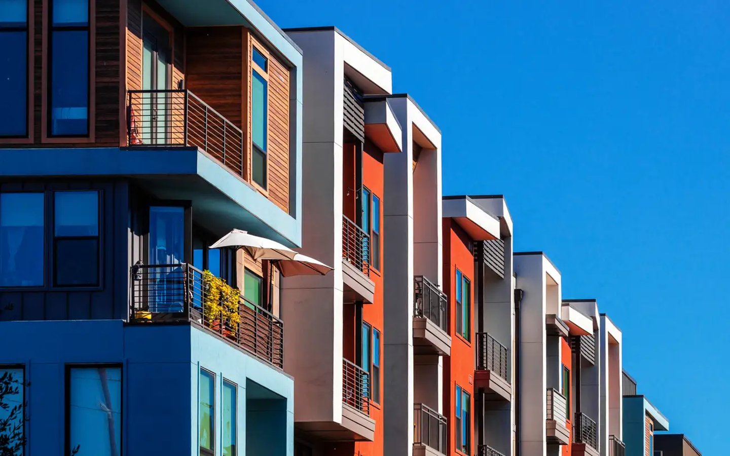 Modern garden-style condo building with colorful facades and balconies against a clear blue sky.