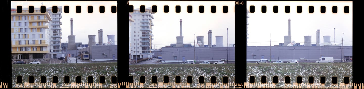 Composed urban photograph showcasing a snowy grassy area with commercial and industrial structures in the background