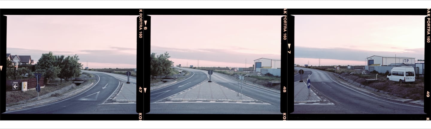 Composed photo of a dusk on a winding road, small buildings in the distance. A white van parked near a building