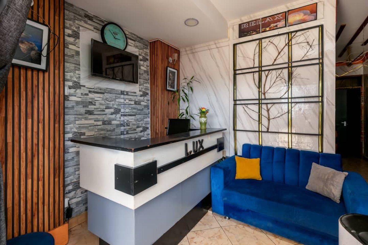 Modern spa reception area with a white marble desk, blue velvet sofa, and stone wall decor.