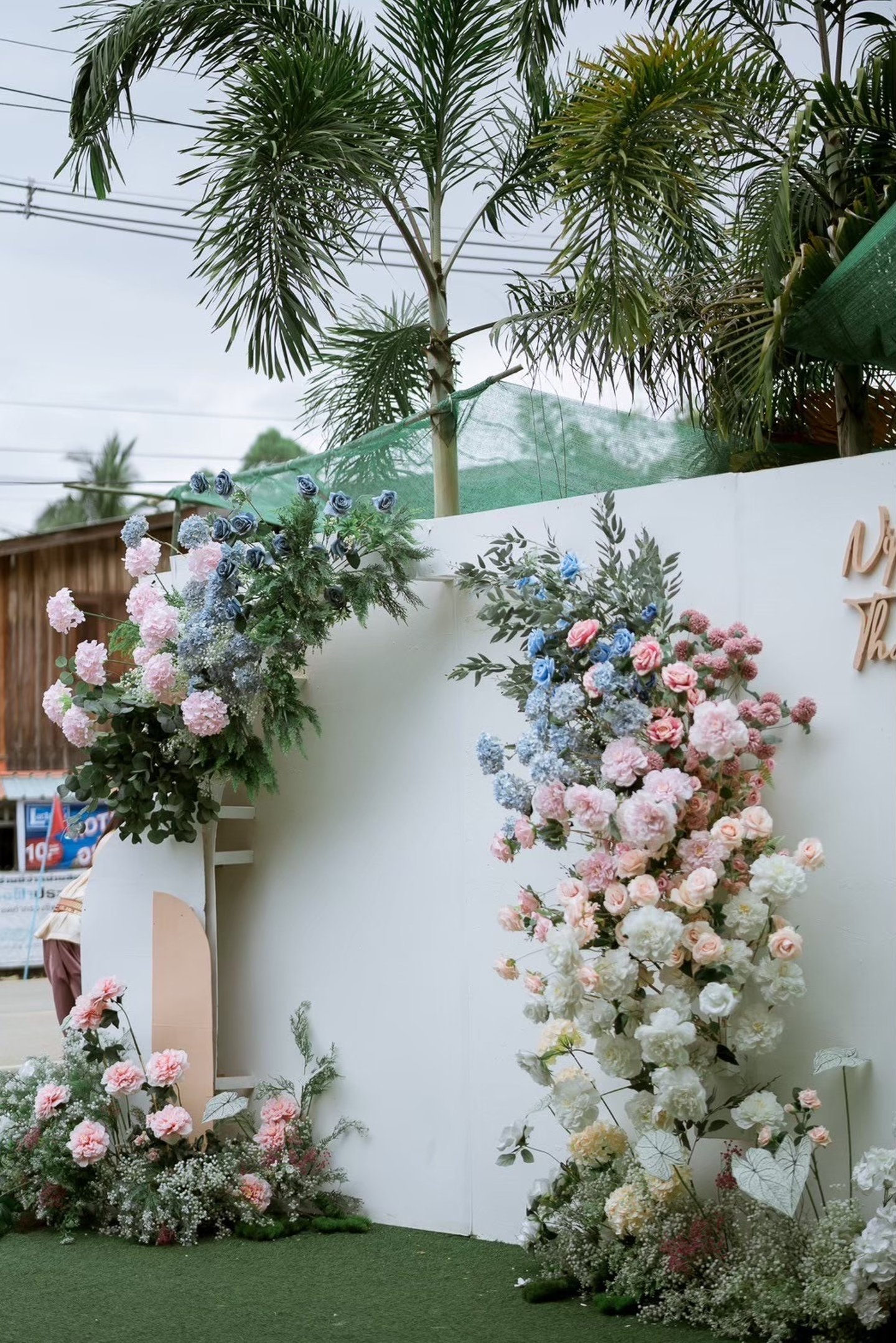 ตกแต่งซุ้มงานแต่งดอกไม้โทนพาสเทลสีชมพูและฟ้า พร้อมป้ายชื่อบ่าวสาว