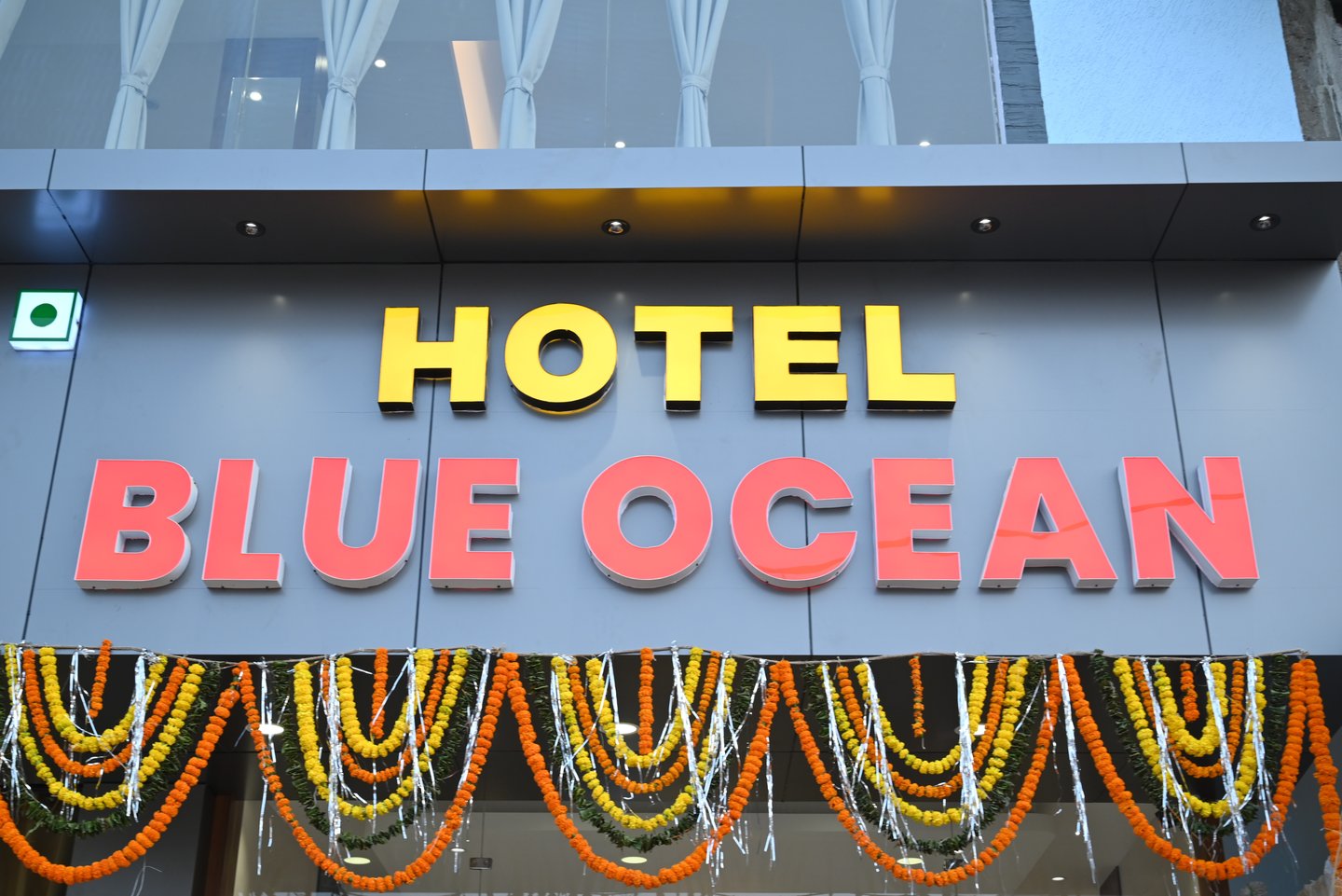 The exterior signage for Hotel Blue Ocean featuring yellow and orange illuminated letters decorated with flower garlands.