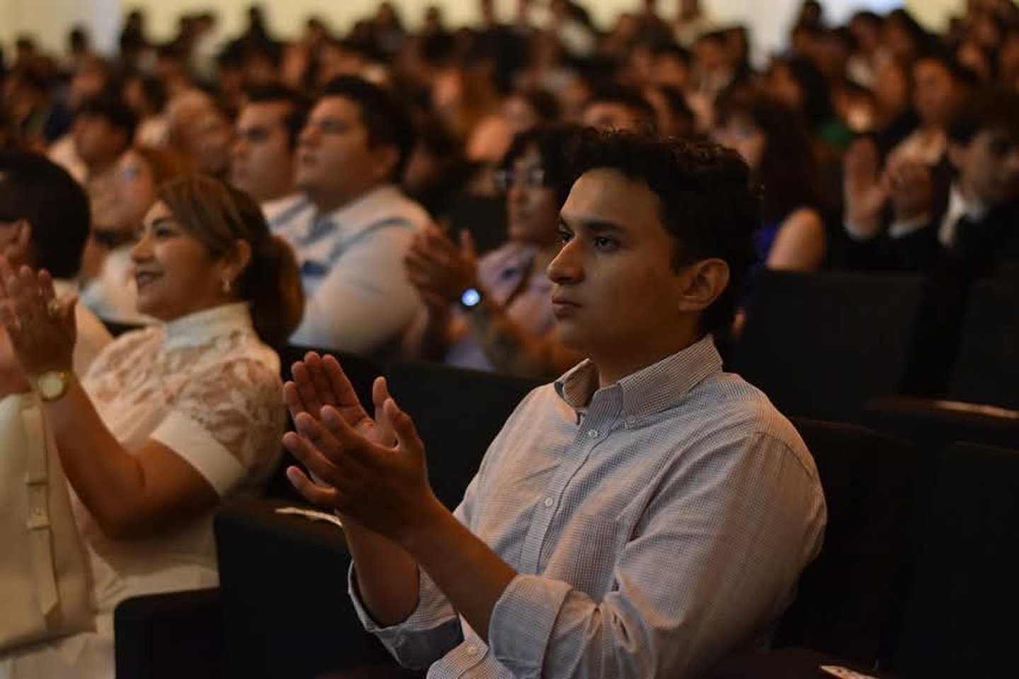 Hombre joven aplaudiendo desde el público con más personas aplaudiendo al fondo