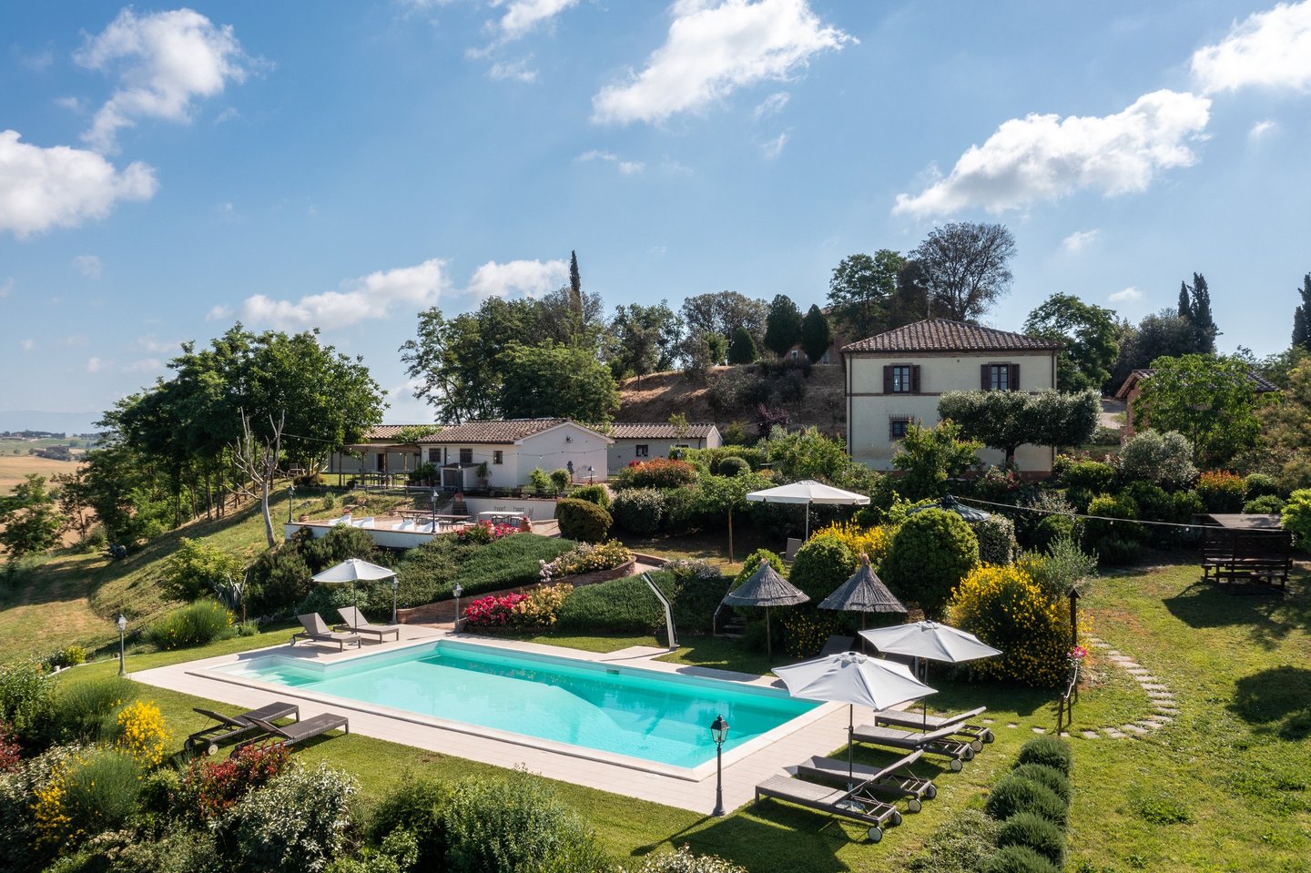 Luxury villa in Tuscany with an outdoor swimming pool, lounge chairs, and lush garden landscape.