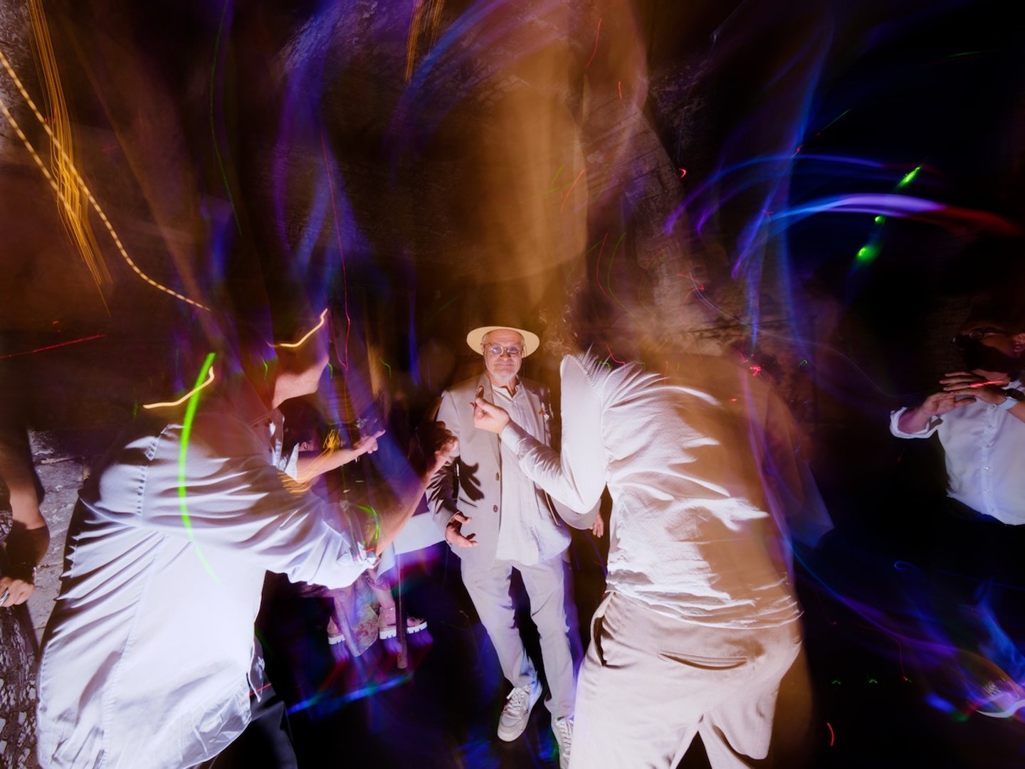 Des invités dansent lors d'une réception de mariage animée, avec de magnifiques effets de traînée lumineuse sur les photos