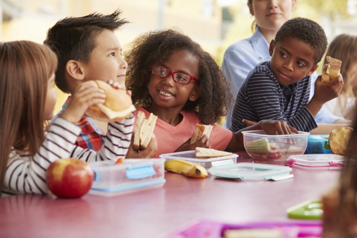 Visually impaired girl enjoying lunch and conversation with classmates in an inclusive school environment.