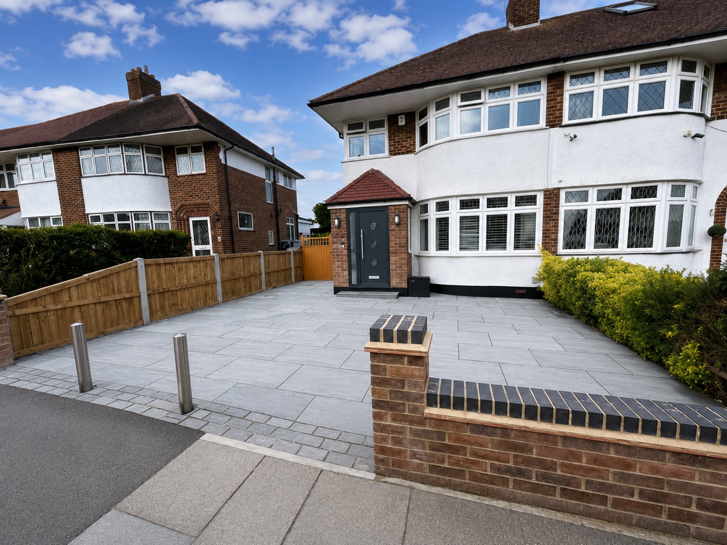 Modern grey stone block paved driveway in front of a white semi-detached house with a new brick wall.