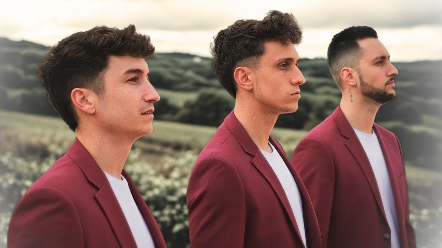 Three men in matching maroon blazers standing in a row against a scenic countryside background.