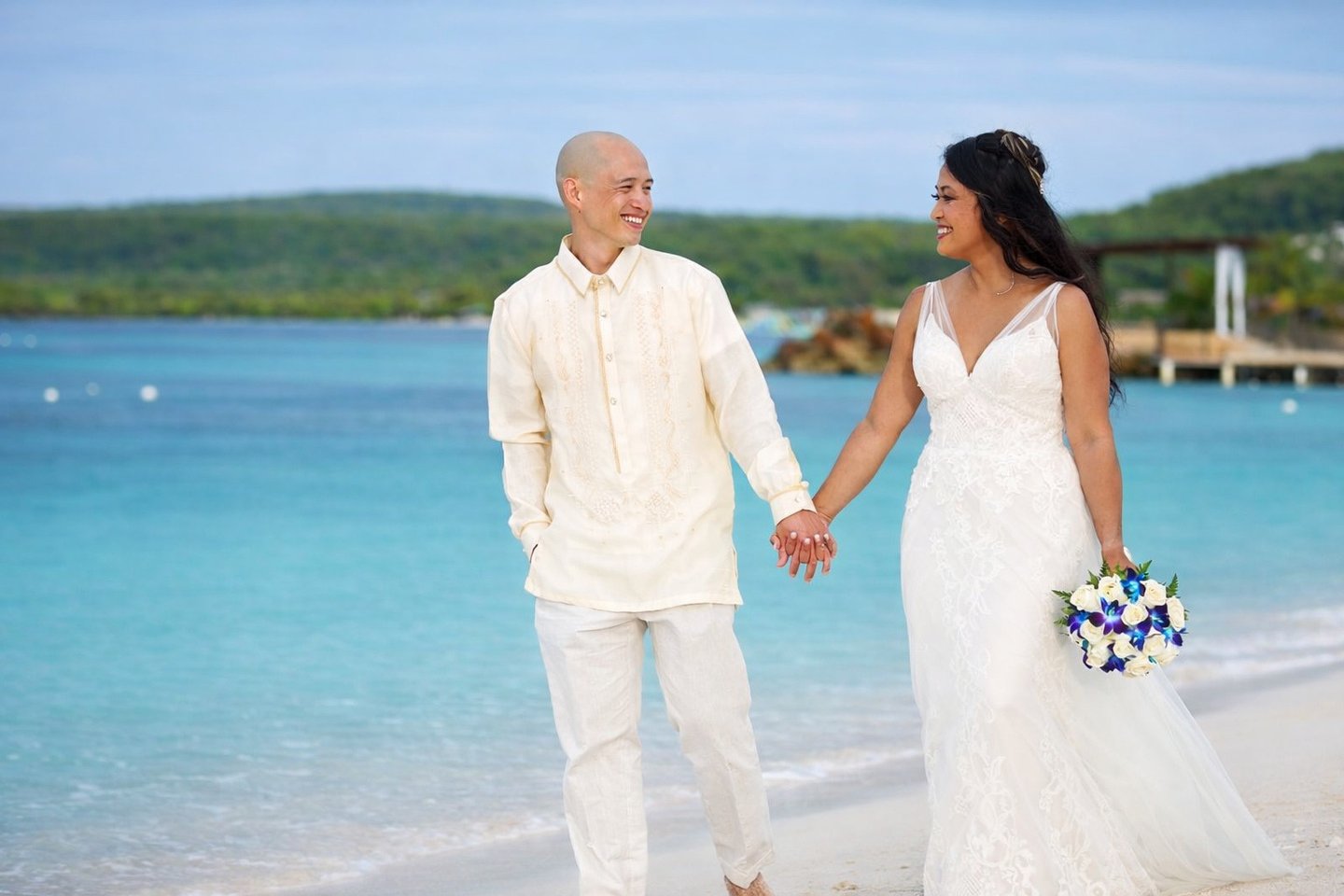 Smiling bride and groom holding hands during a tropical beach wedding ceremony in Jamaica.