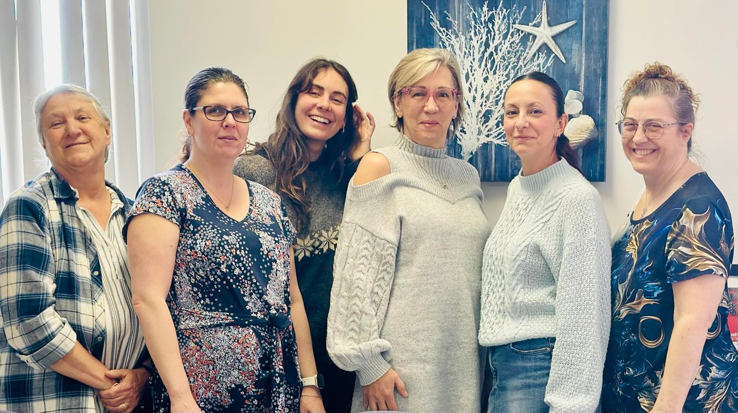 Six smiling professional women posing together in an office with coastal decor.