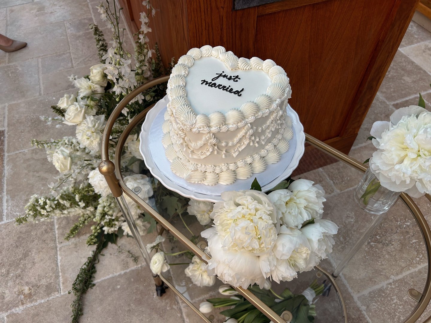 Heart-shaped vintage wedding cake with white frosting and 'just married' script on a gold cart.