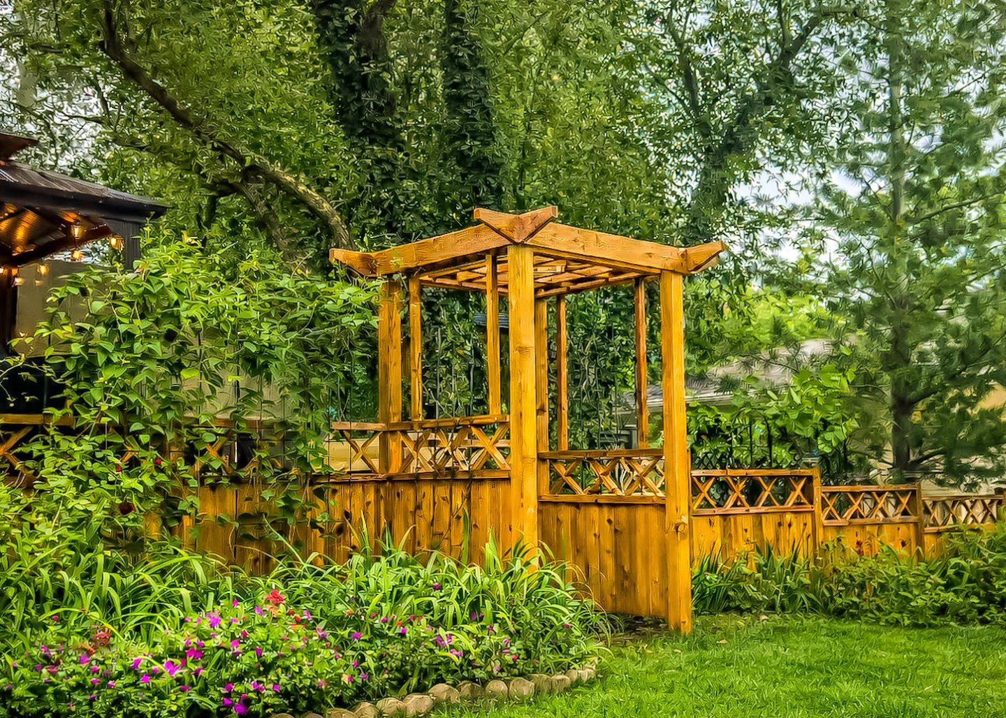 Wooden garden pergola and lattice fence surrounded by lush green plants and colorful flowers.