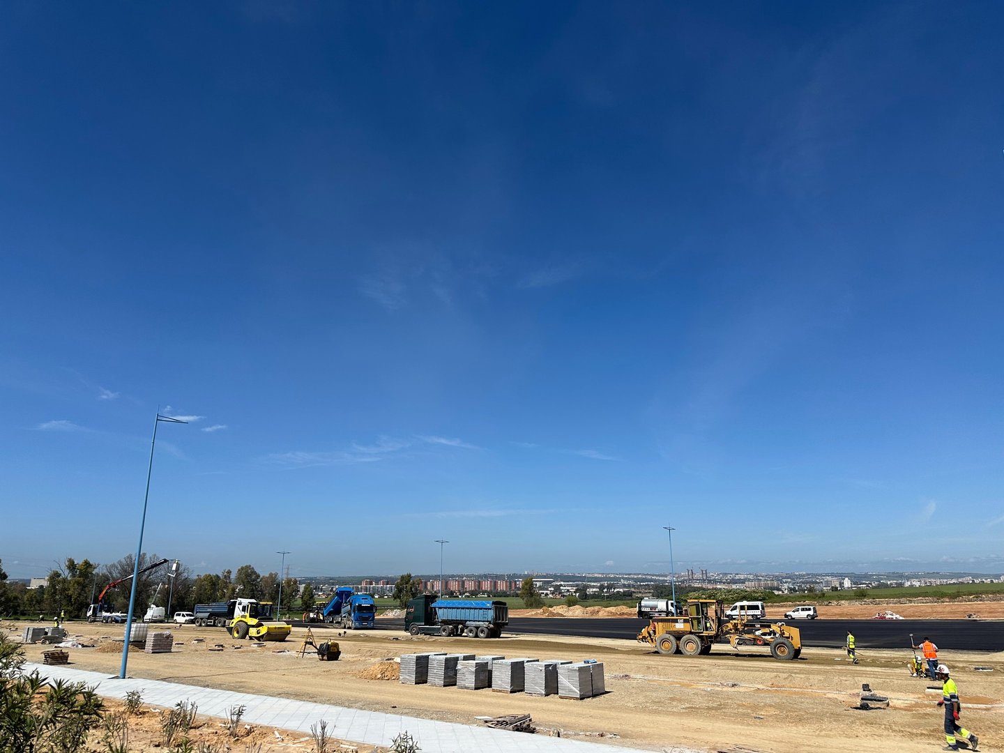 Obra civil en ejecución con extendido de firme asfáltico y maquinaria trabajando en entorno urbano andaluz.