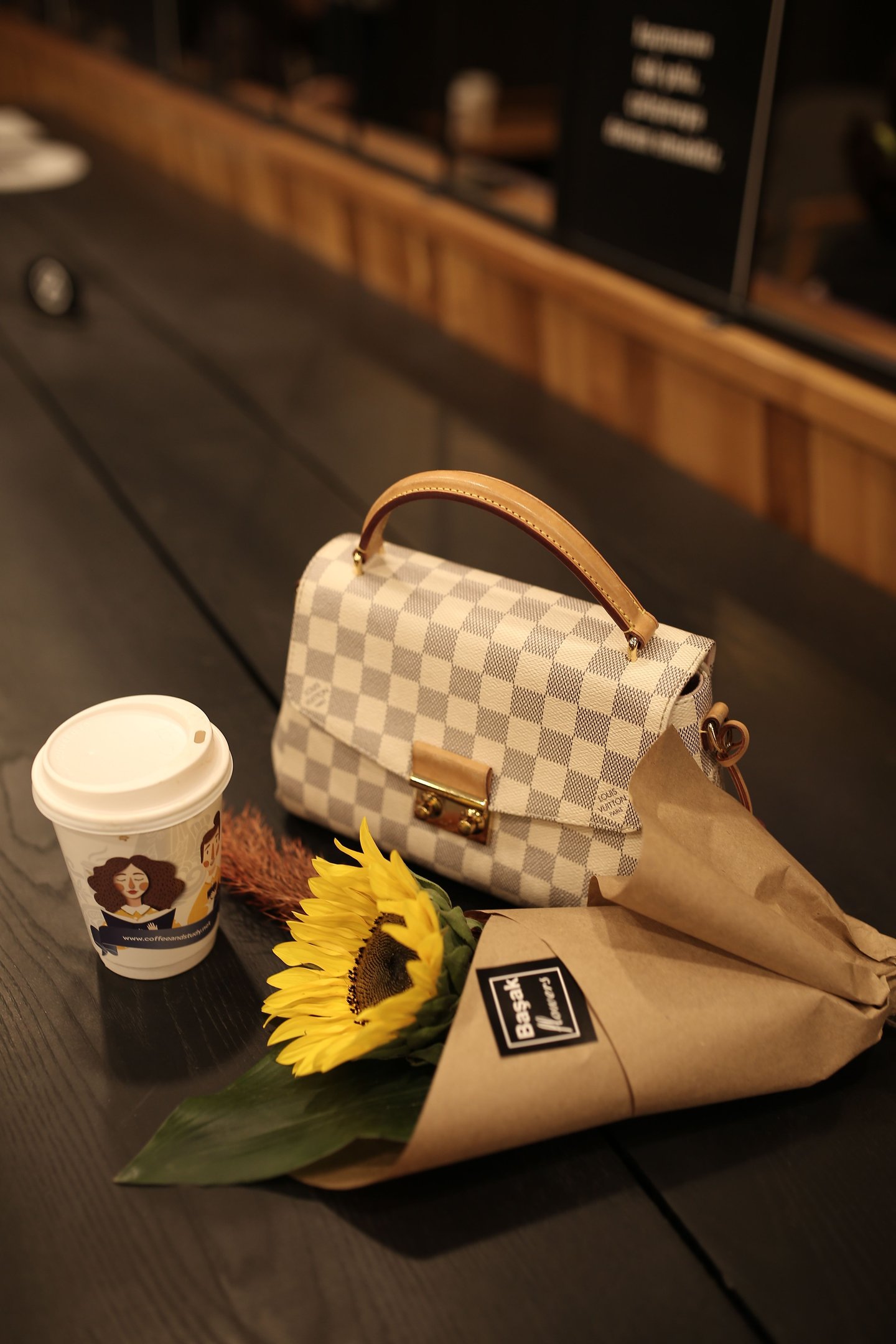Sac Louis Vuitton posé sur une table avec un gobelet et une fleure