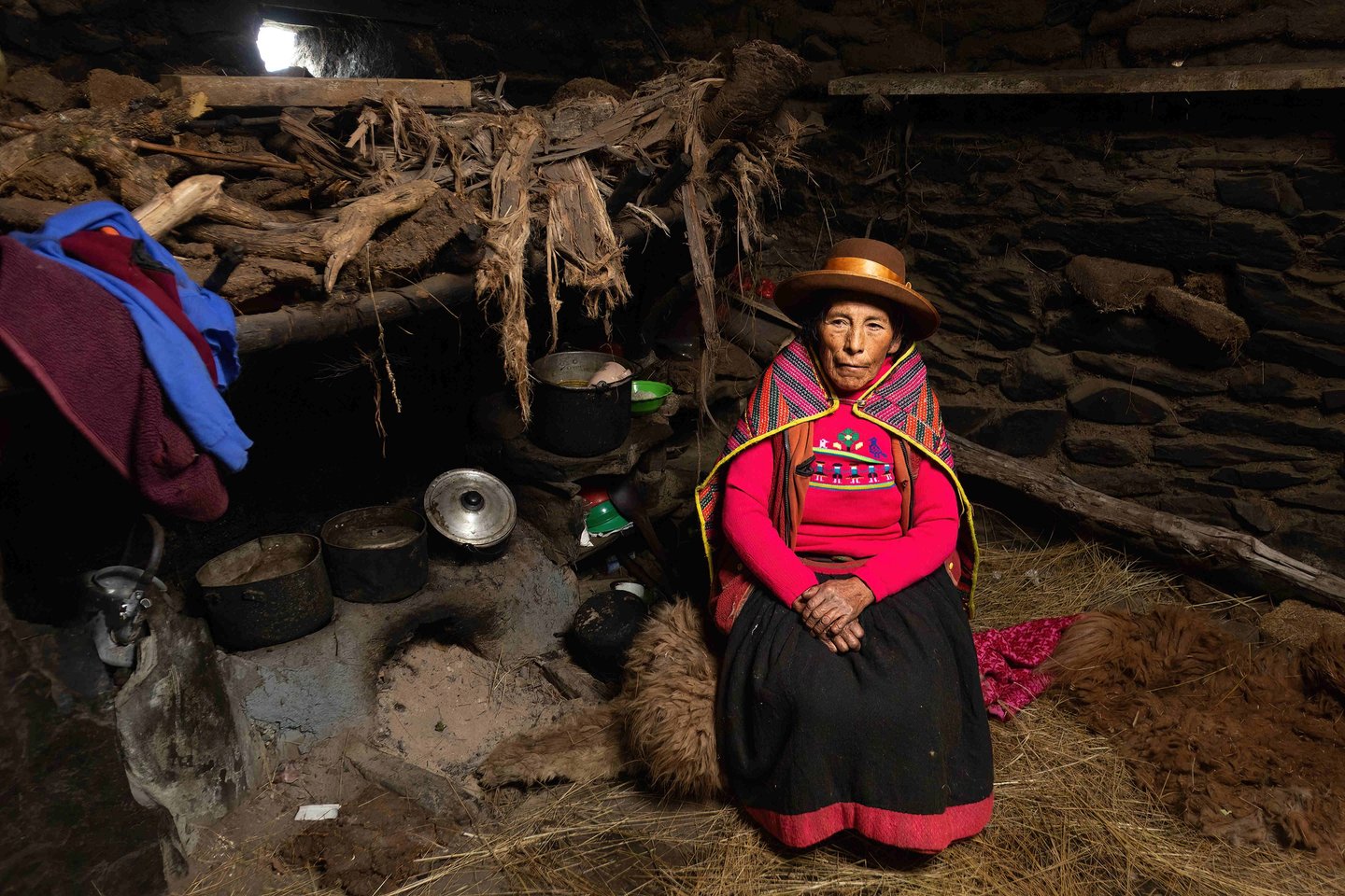 This image captures traditional life in the Peruvian Andes, showing a Quechua woman inside her rustic stone home.