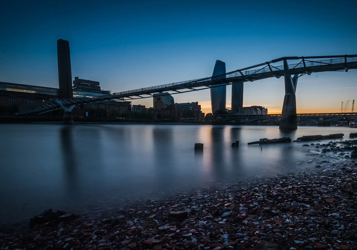London's Millennium Bridge and Tate Modern silhouette over River Thames during a blue hour sunset.