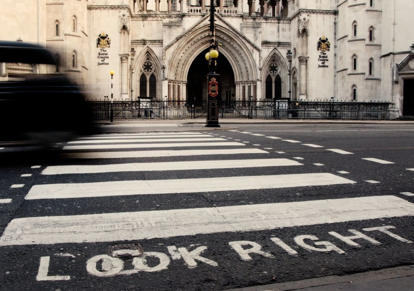 London taxi crossing a zebra pedestrian crossing in front of the Royal Courts of Justice, with “LOOK RIGHT” painted on road