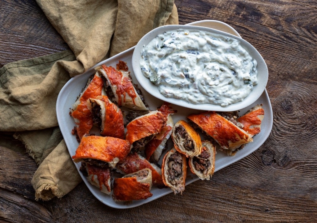 Plate of phyllo beef wellington bites with spinach dip by Dan Clapson