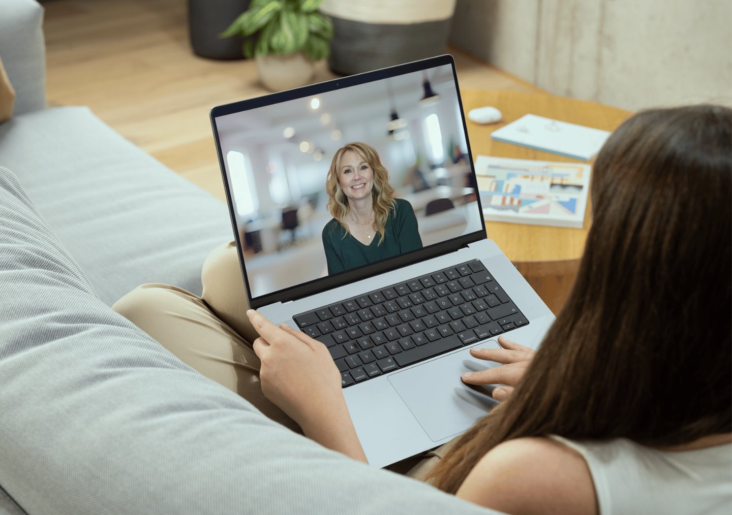 a woman sitting on a couch with a laptop computer screen showing a video chat with Gina Danford