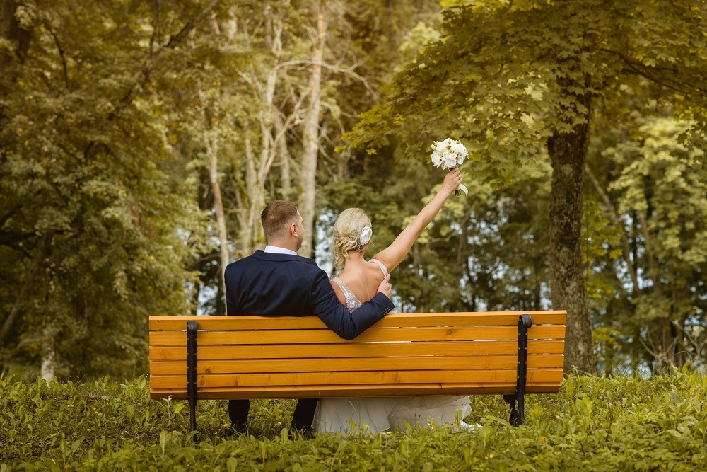 a bride and groom sitting on a bench in a park