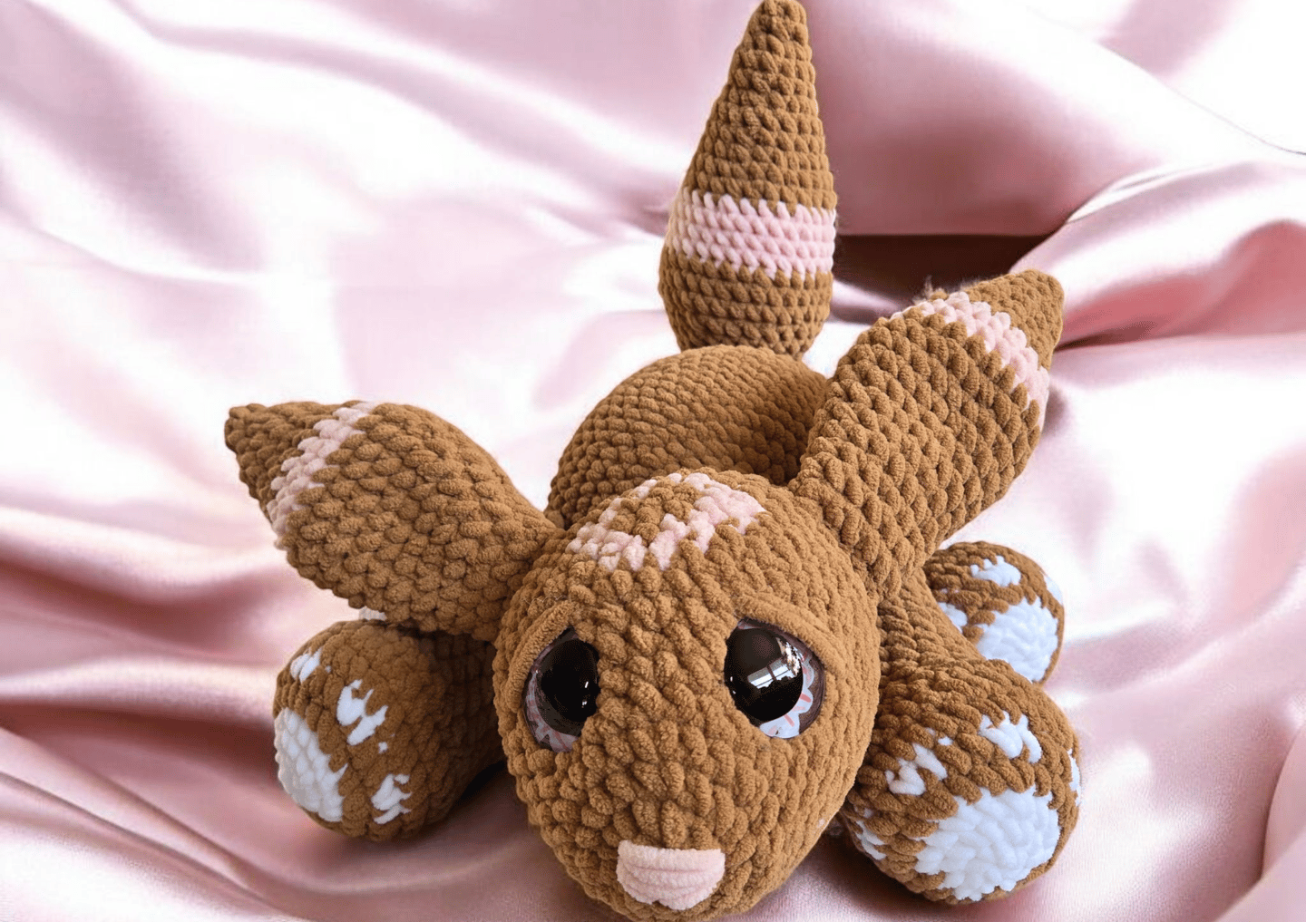 Handmade brown velvet bunny plushie with pink and white details, laying on soft pink satin fabric