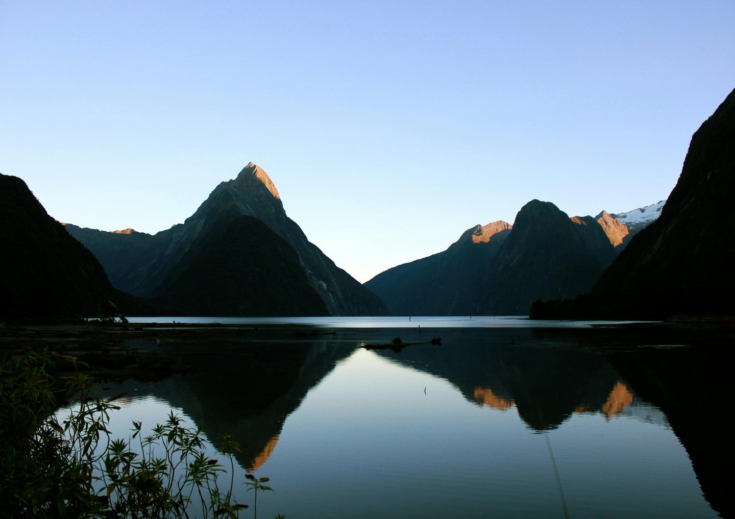 Milford Sound mountains reflected in calm water at sunrise in Fiordland National Park, New Zealand.