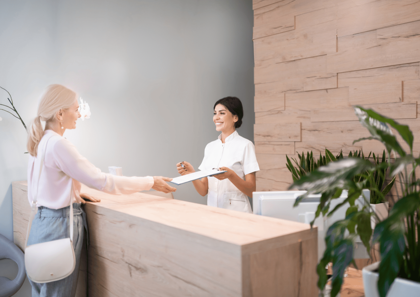 una mujer con camisa blanca de pie en el mostrador de recepción de una clínica dental