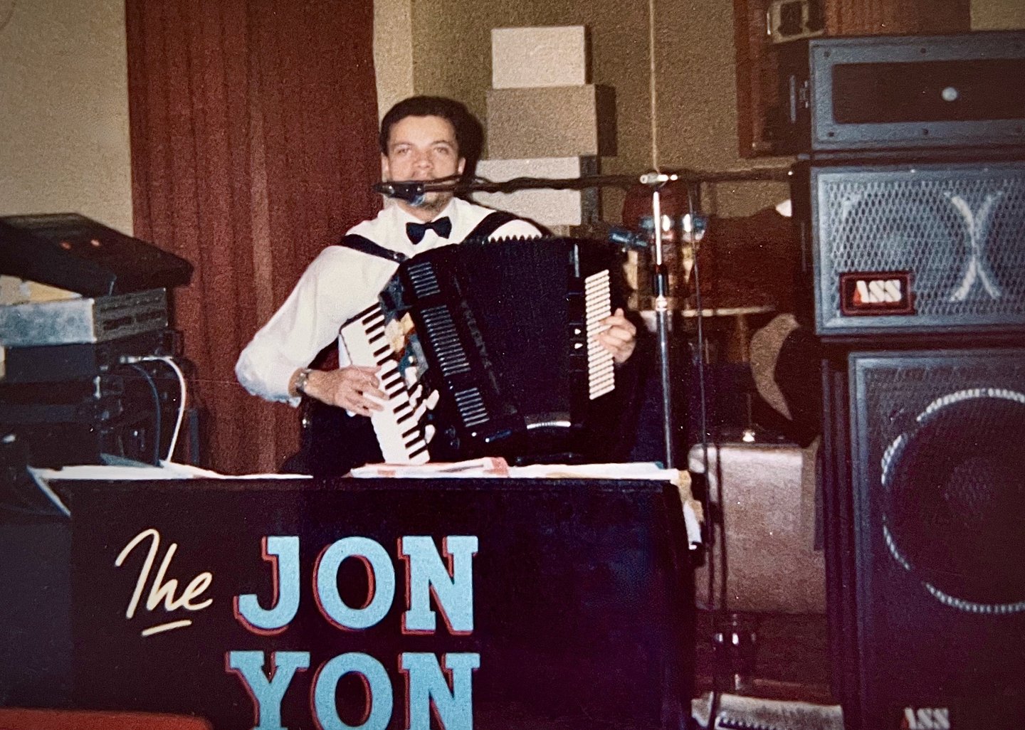 Jon Yon playing and singing live with his electronic accordion, surrounded by a stack of speakers.