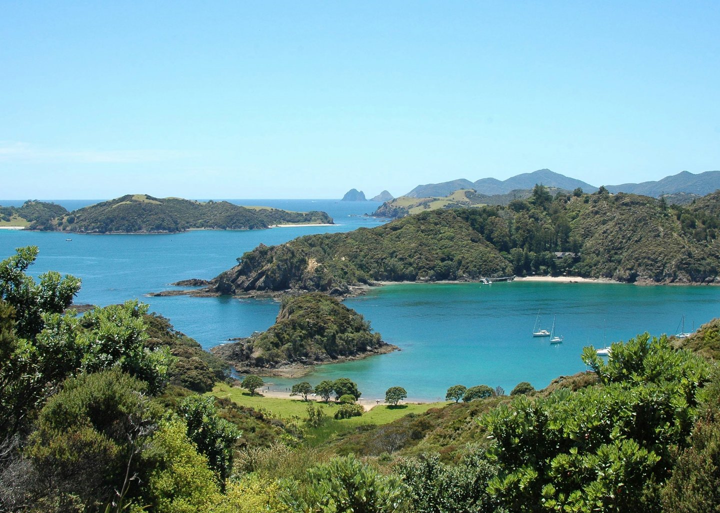 Aerial view of tropical islands and blue water in the Bay of Islands, New Zealand, with boats and lush greenery.