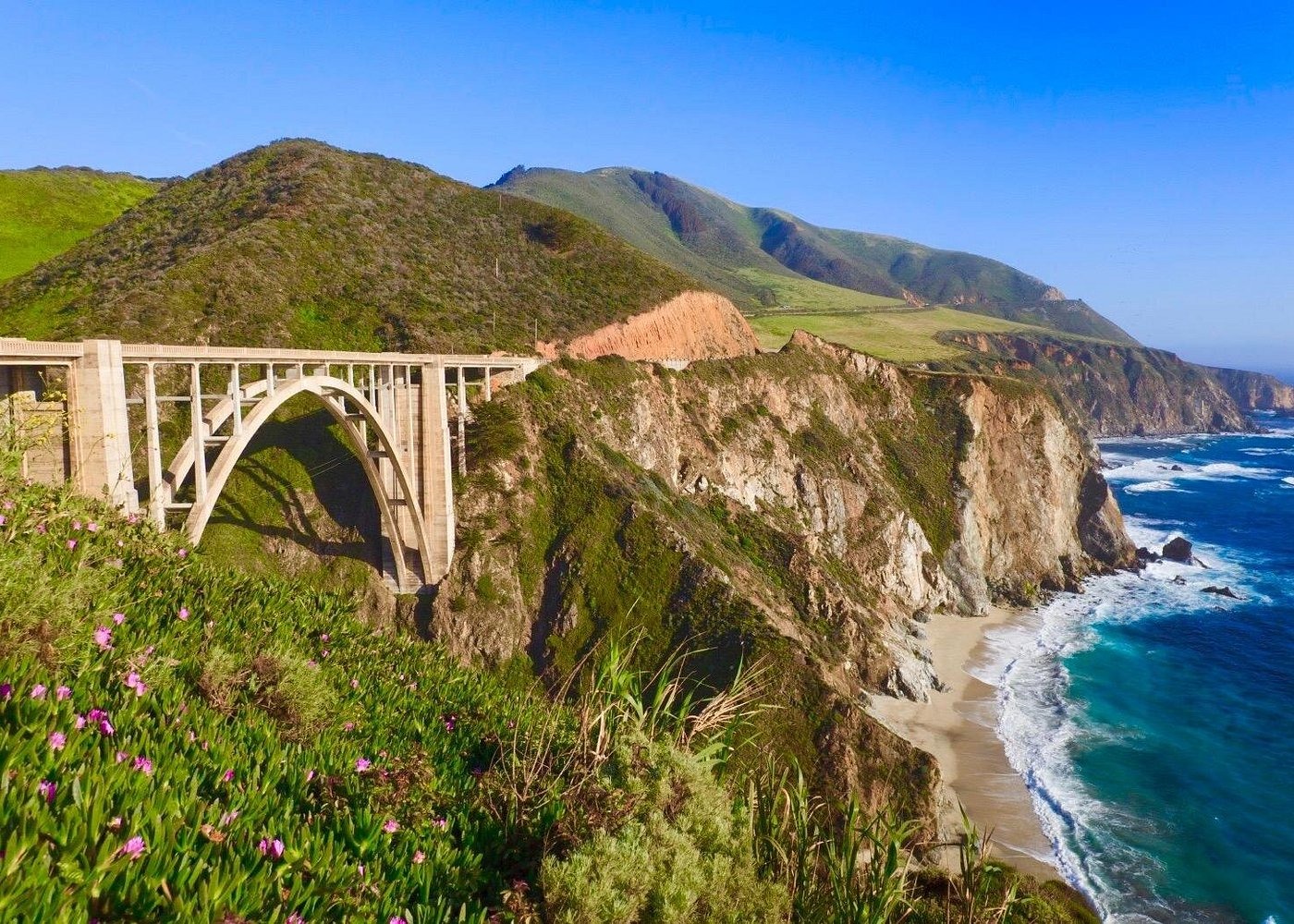 Bixby Creek Bridge on the Big Sur coast of California with ocean waves and green cliffs.