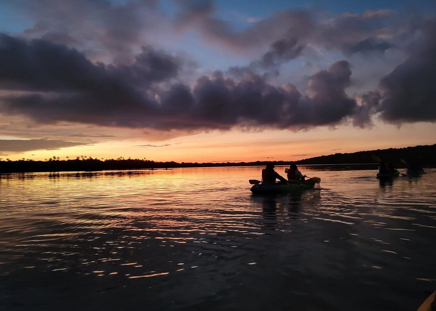 Two people in a kayak enjoy a calm sunset paddle on a wide river with golden reflections.