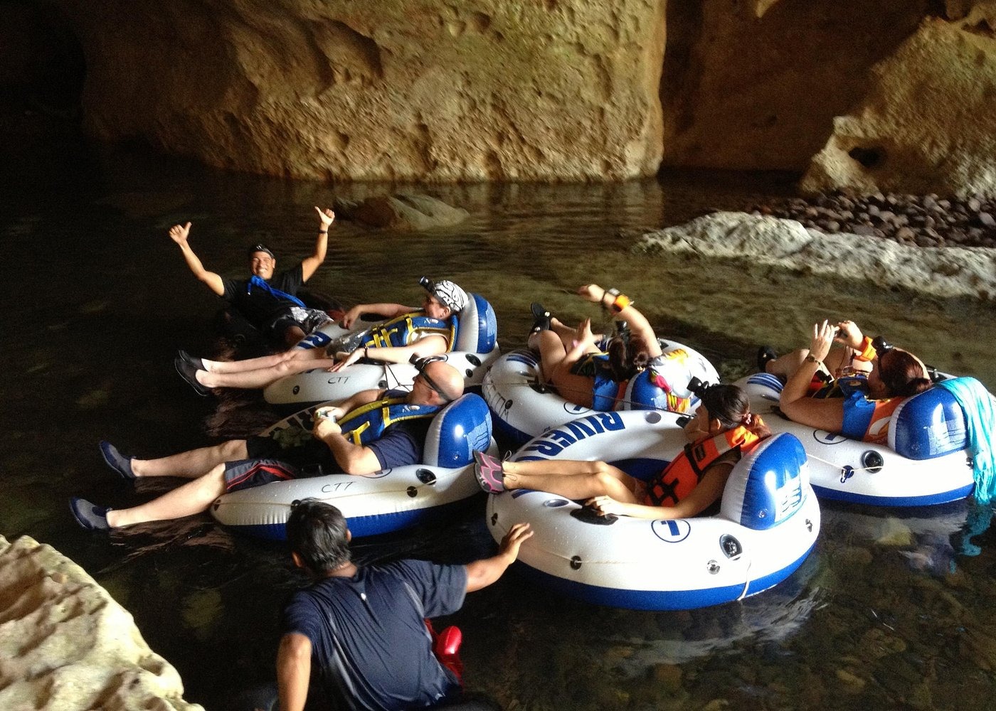 A group of tourists wearing life jackets and cave tubing in an underground river cave in Belize.