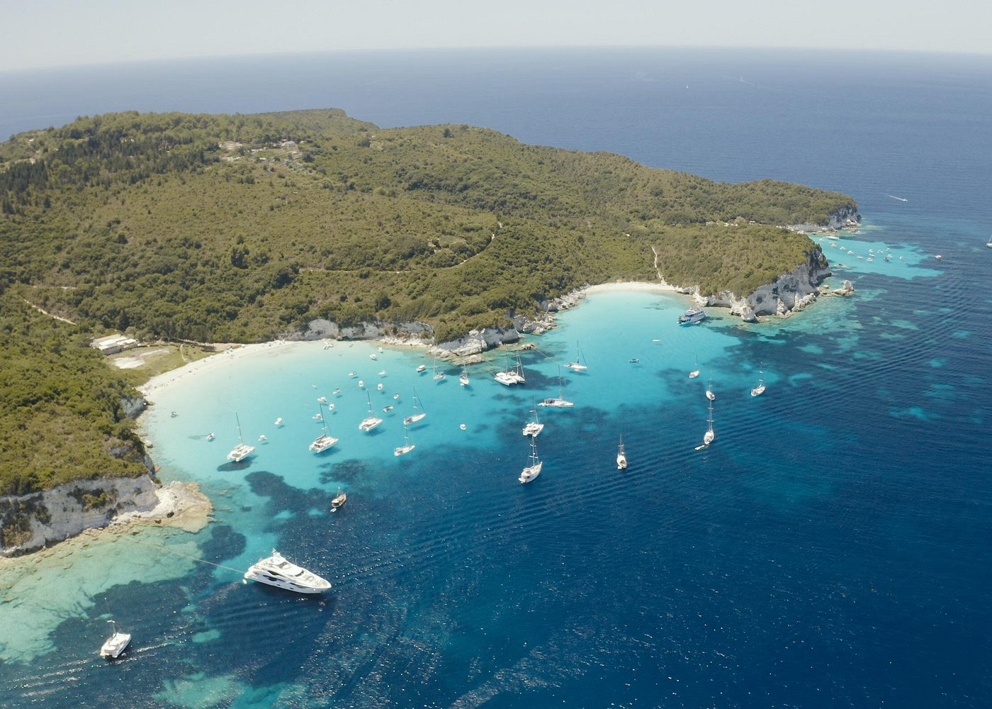 Aerial view of white yachts and sailboats anchored in the turquoise waters of a tropical island bay.