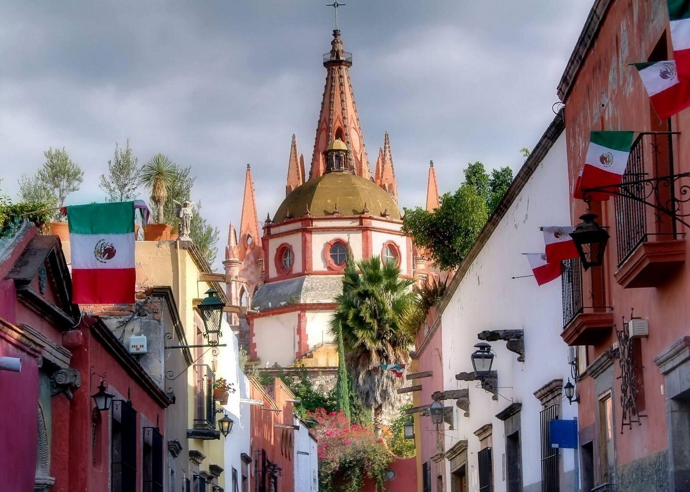 Street view of colonial buildings with Mexican flags and the Parroquia cathedral in San Miguel de Allende.