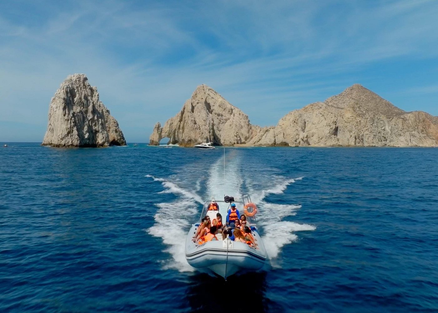 Tourists on a motorboat cruise toward the Arch of Cabo San Lucas in Mexico's blue waters.