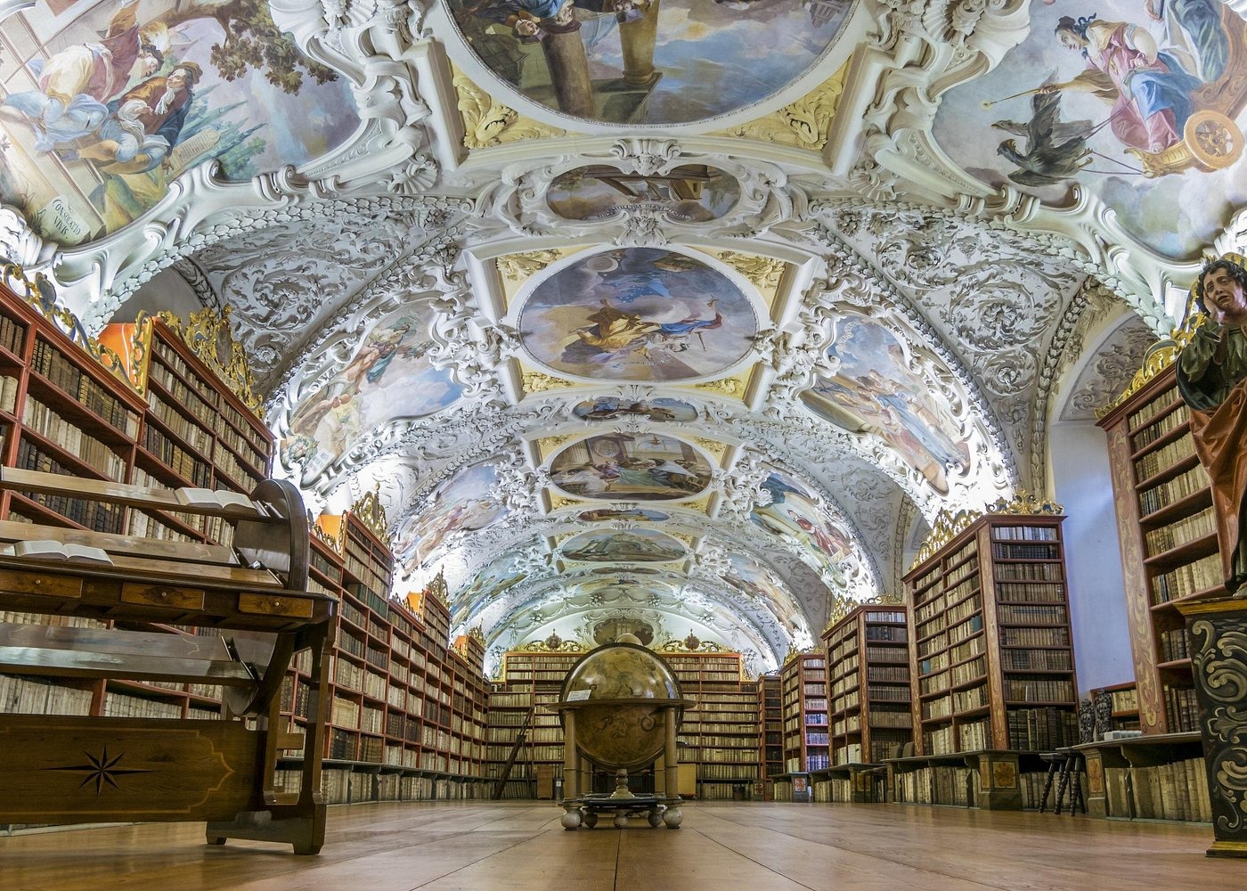 Ornate Baroque ceiling frescoes in the historic Strahov Monastery library with ancient bookshelves and a globe.